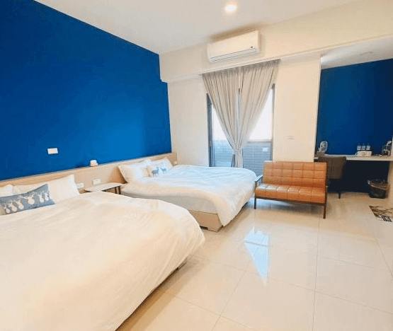 【鹿港住宿】溫怡鹿鹿WinLuLu的雙床房，牆面上的藍色背景牆使房間顯得更加醒目。窗戶旁的座位區域提供了放鬆的角落，並有桌椅設置，讓人可以輕鬆辦公或享受悠閒時光。