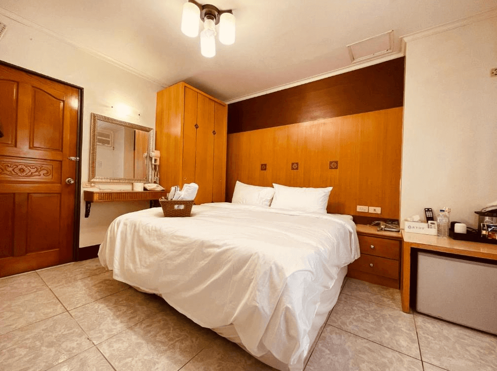 【四重溪溫泉】舍下立宇溫泉的雙人房，設有一張大床，搭配木質床頭牆與暖色調燈光，營造舒適的氛圍。房內配備梳妝台、掛鏡、木製衣櫃與床頭櫃，提供充足的收納空間。此外，備有小冰箱、茶壺與迎賓點心，提供便利的住宿體驗。