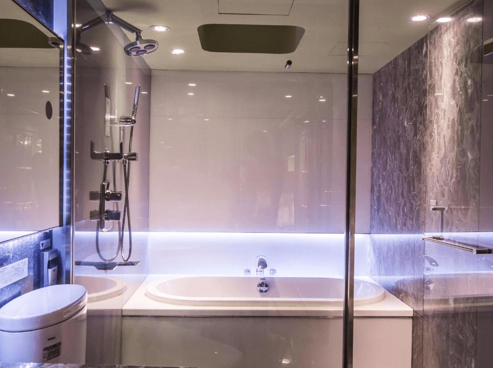 【西門町住宿】薆悅酒店西寧館現代感十足的浴室，設有大型浴缸與玻璃淋浴間。浴室牆面採用大理石紋理與鏡面設計，搭配隱藏式LED燈條營造高級感。配備多功能淋浴設備與免治馬桶，提供舒適的沐浴體驗。