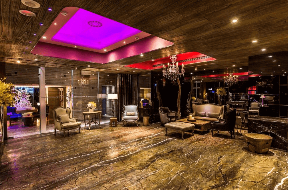 【西門町住宿】薆悅酒店西寧館的華麗典雅飯店大廳，地面鋪設黑金大理石，搭配木質天花板與水晶吊燈，呈現奢華氛圍。空間內擺放多組高背沙發與復古家具，並以紫色燈光點綴天花板，提升整體視覺效果。