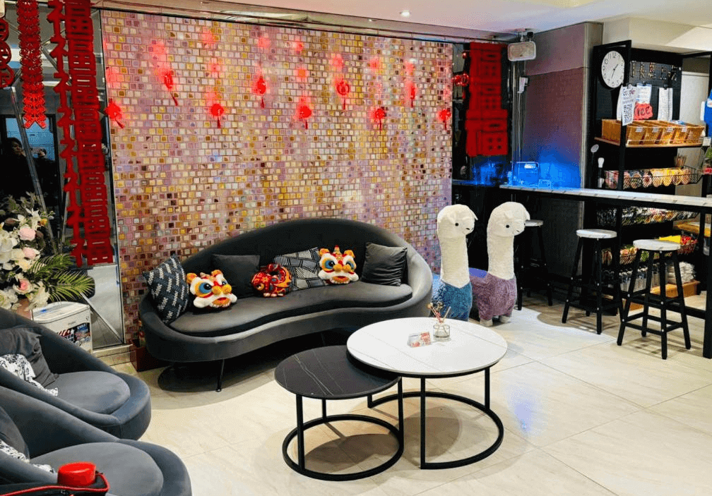 【松山機場住宿】「豪城商旅民生館」大廳一景，設計融合中式與現代元素，牆面裝飾有紅色燈籠與「福」字掛飾，營造喜氣洋洋的氛圍。黑色圓弧沙發搭配可愛的羊駝玩偶，並設有自助吧檯與販賣區，提供旅客輕食與飲品選擇。