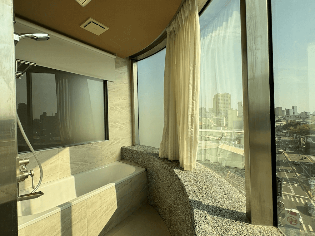 【台北親子飯店】路境行旅的景觀浴室，設有大面積落地玻璃窗，可俯瞰城市街景。浴室內設有浴缸與淋浴設備，搭配自然採光，讓旅客享受放鬆的泡澡時光，同時欣賞窗外風景。