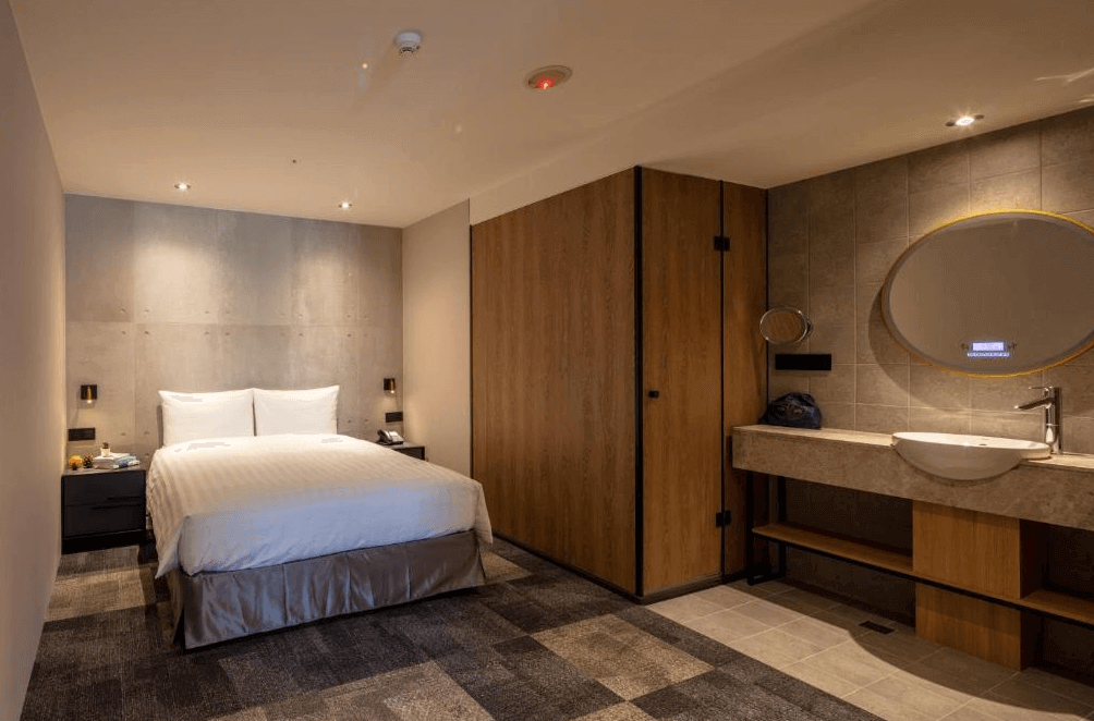 【台北車站住宿】路徒Plus行旅 主題館工業風格設計的雙人房，房內擁有一張大床與混搭木質與水泥牆面，結合開放式衛浴空間。浴室區域設有大型圓鏡、石質洗手台與木質置物空間，呈現時尚前衛的住宿體驗。