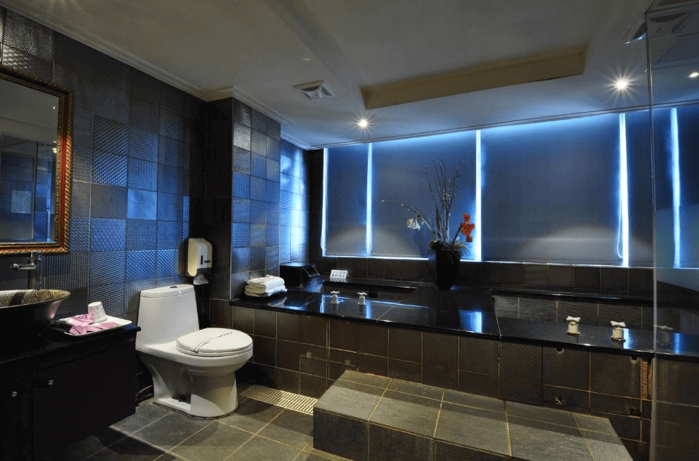 【金山溫泉】金湯溫泉會館的高級衛浴空間，採用深色石材打造長型溫泉池，並搭配柔和燈光，營造靜謐放鬆的泡湯環境。浴室內配有大型鏡面、馬桶與現代化洗手台，整體風格典雅且奢華，適合享受私人泡湯時光。