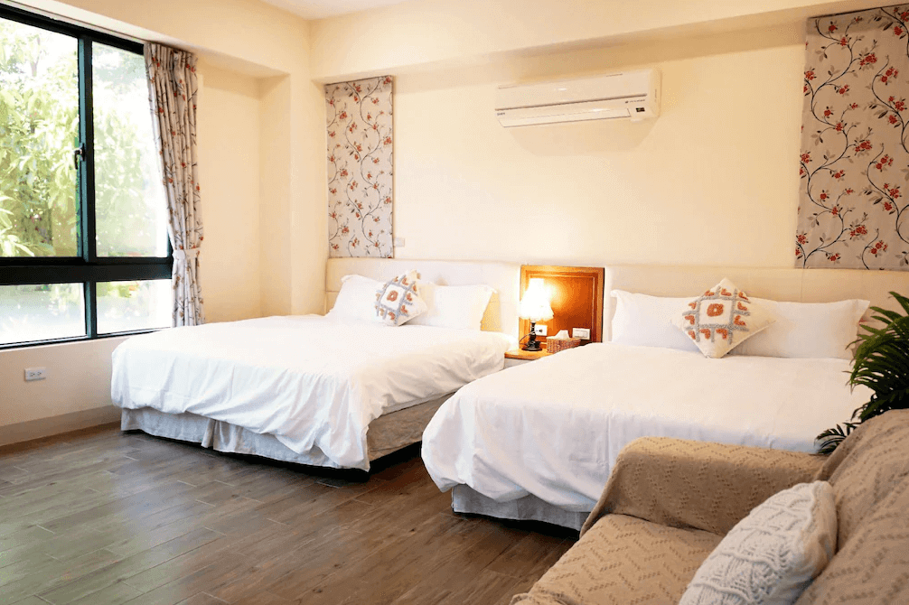 【集集火車站住宿】陶花巷弄民宿的雙床房，設有兩張舒適的雙人床，床上擺放著精緻的抱枕，房間內有大窗戶可欣賞外面的綠意，空調及床頭燈提供額外的舒適感。