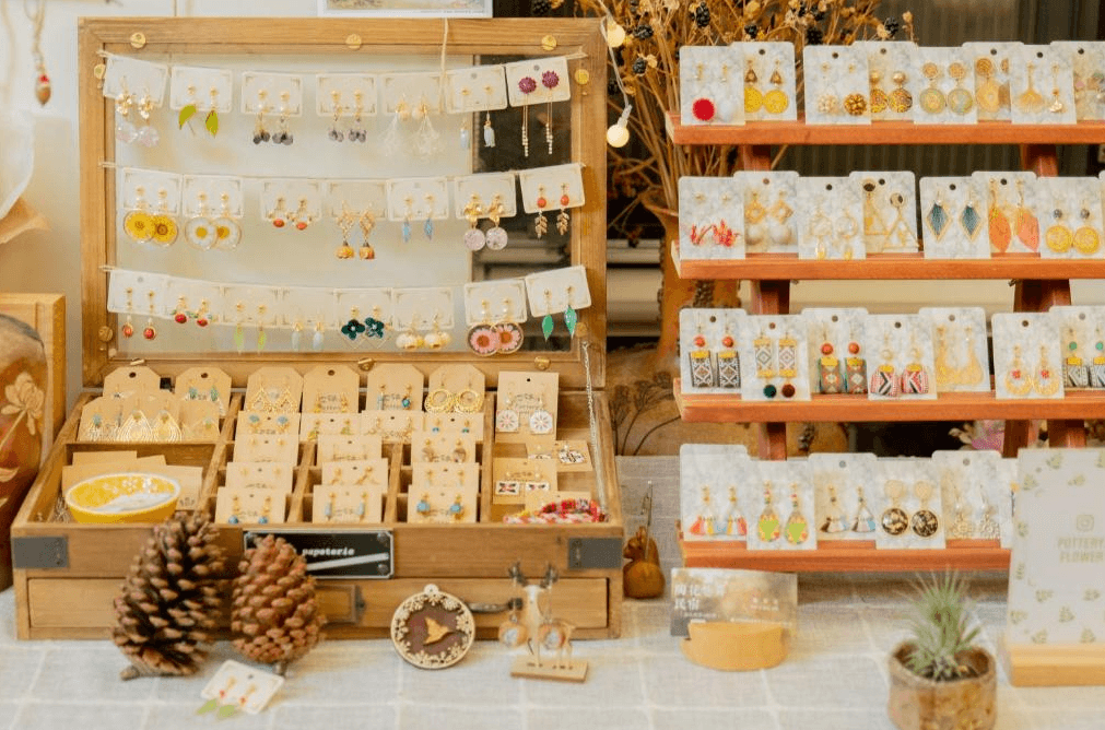【集集火車站住宿】陶花巷弄民宿的手工耳環，擺放在木質展示架上，配以精心設計的標籤，周圍還有小巧的裝飾品，如松果與小植物，營造出溫馨的手作氛圍。