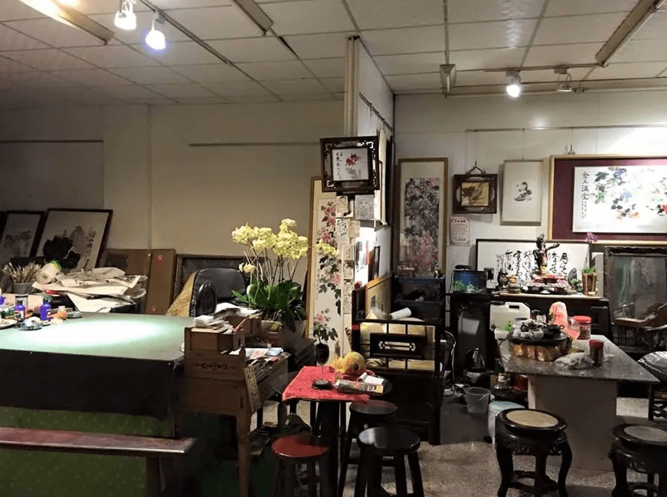 【集集火車站住宿】集集藝術家背包客之家藝術氛圍濃厚的工作坊或公共空間，擺放著大量的書畫、藝術品與文房四寶，桌上還有未完成的書畫作品。牆上懸掛多幅水墨畫與書法作品，使整體空間充滿傳統文化與藝術氣息，適合藝術愛好者交流與創作。