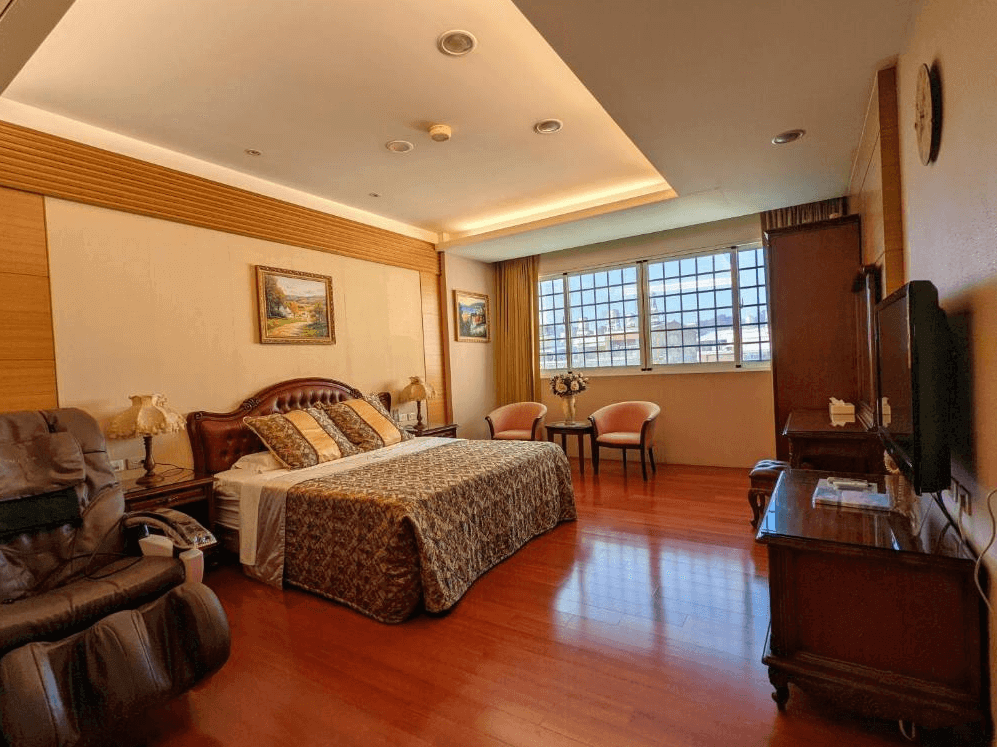 歐式古典風格的雙人房，設有雕花木質床架與華麗床單，搭配典雅的床頭燈與掛畫，營造高貴優雅的住宿氛圍。房內配有按摩椅、木質地板及大片窗戶，自然採光充足，讓空間更加明亮舒適。