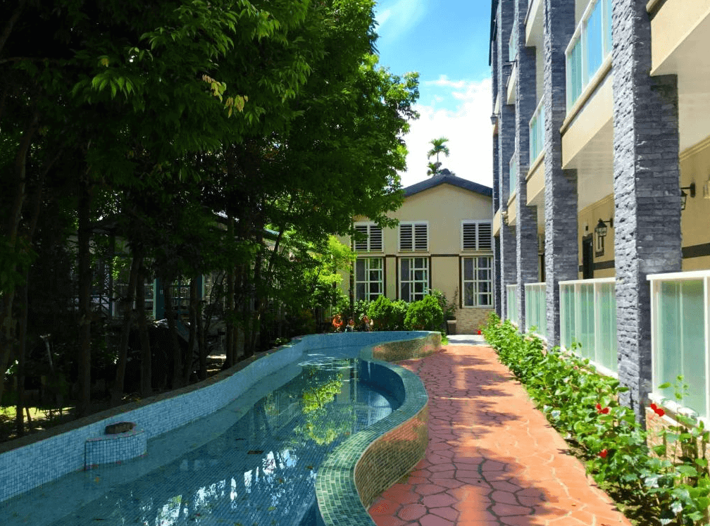 【集集火車站住宿】香榭雅筑民宿的戶外庭院，設有蜿蜒的水池與綠意盎然的花園步道，兩側建築以歐式石磚裝飾，營造高雅靜謐的氛圍。庭院內綠樹成蔭，提供旅客一個放鬆休憩的理想空間，感受悠閒自在的住宿體驗。