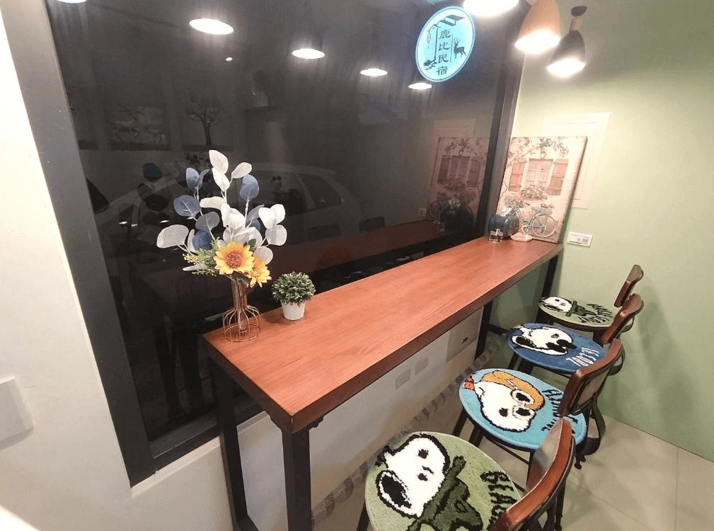 【鹿港住宿】鹿比民宿充滿趣味設計的用餐區。這裡有一個長桌和可愛的椅墊，椅墊上印有漫畫人物的圖案，增添了房間的可愛氛圍。這個小型的區域不僅有藝術感，還具有實用功能，為住客提供了一個輕鬆聚會的場所。