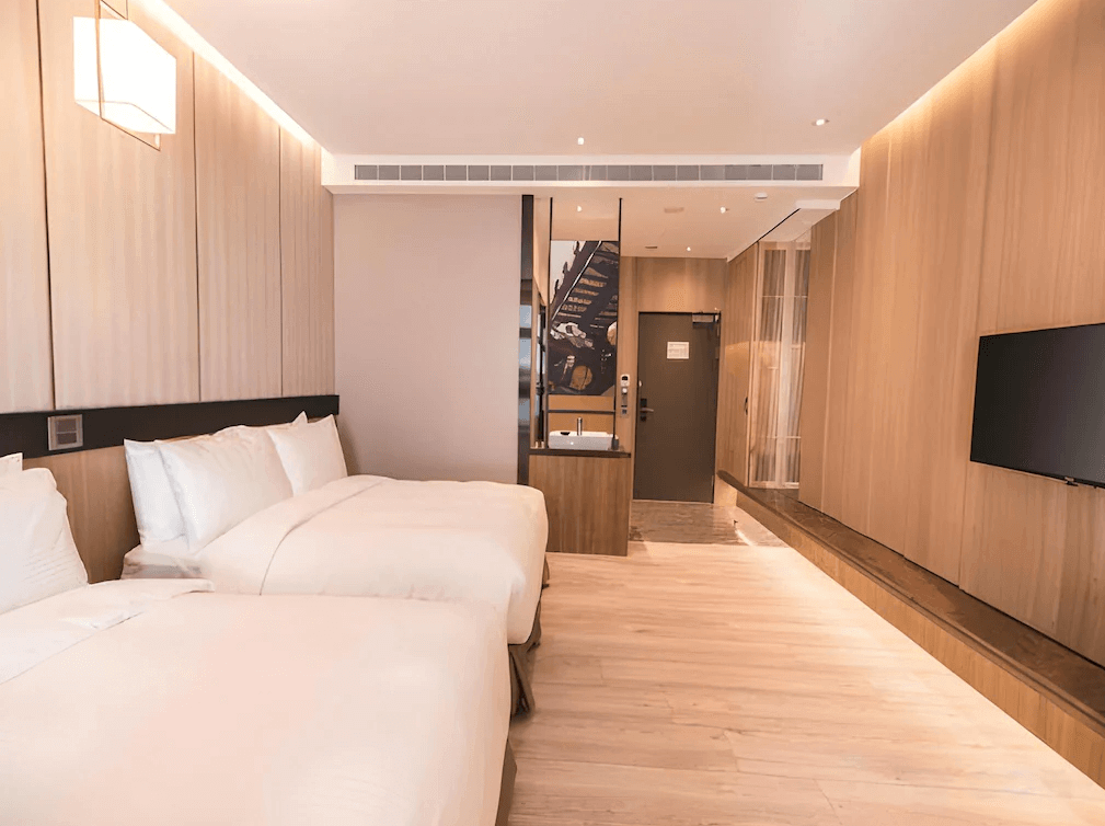 【鹿港住宿】鹿港澄悅酒店的雙床房，牆面使用了木質元素和柔和的照明，營造出溫馨的氛圍。房間內設有兩張床和一個簡約的工作區，窗邊有一個舒適的座位區，讓住客可以放鬆或欣賞外面的景觀。