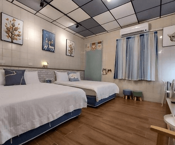 【鹿港住宿】鹿鹿咪民宿的房間，配有兩張床和舒適的枕頭，牆面裝飾有插圖，窗簾呈現清新的藍色調。房間內有簡約現代的家具，並充滿著放鬆的氛圍。