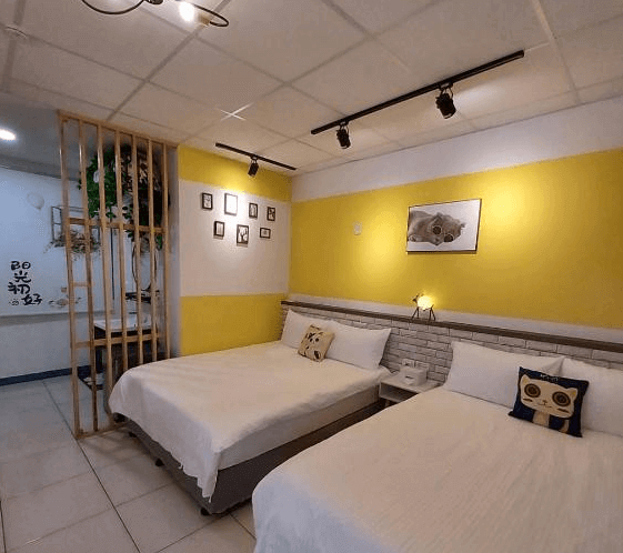 【鹿港住宿】鹿鹿咪民宿的黃色牆面房間，搭配俏皮的抱枕和簡潔的床鋪，房間內的植物和裝飾品增添了一絲自然的氣息。設計簡約，營造出輕鬆愉快的居住感受。