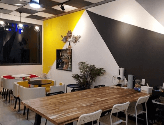 【鹿港住宿】鹿鹿咪民宿的公共空間，設有寬敞的餐桌和多種座位選擇，牆面用幾何圖形裝飾，色調融合了鮮明的黃色與黑色，提供舒適的社交空間。