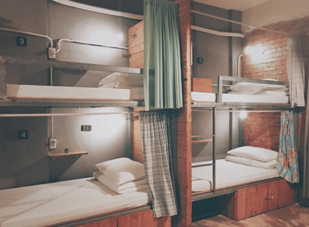 【台中背包客棧】"台中背包客棧精選示意圖"62巷背包客棧的宿舍房，採用金屬與木質結合的上下鋪設計，每張床位都有插座、獨立閱讀燈與小型置物架，並搭配不同色調的遮簾提升隱私感。紅磚牆與裸露管線賦予房間濃厚的工業復古風，營造出獨特的住宿氛圍。