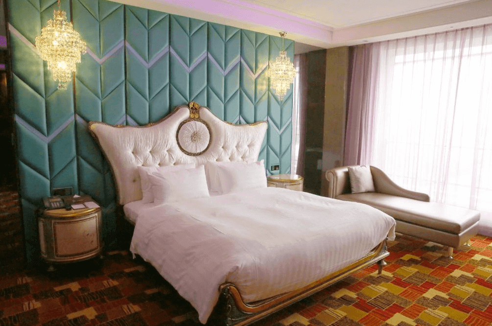 【斗六住宿】三好國際酒店華麗風格的雙人房，設有雕花床架與絨布床頭板，背景為綠松石色立體牆面，搭配兩盞水晶吊燈與大型落地窗，窗邊配有貴妃椅，整體風格高貴典雅。