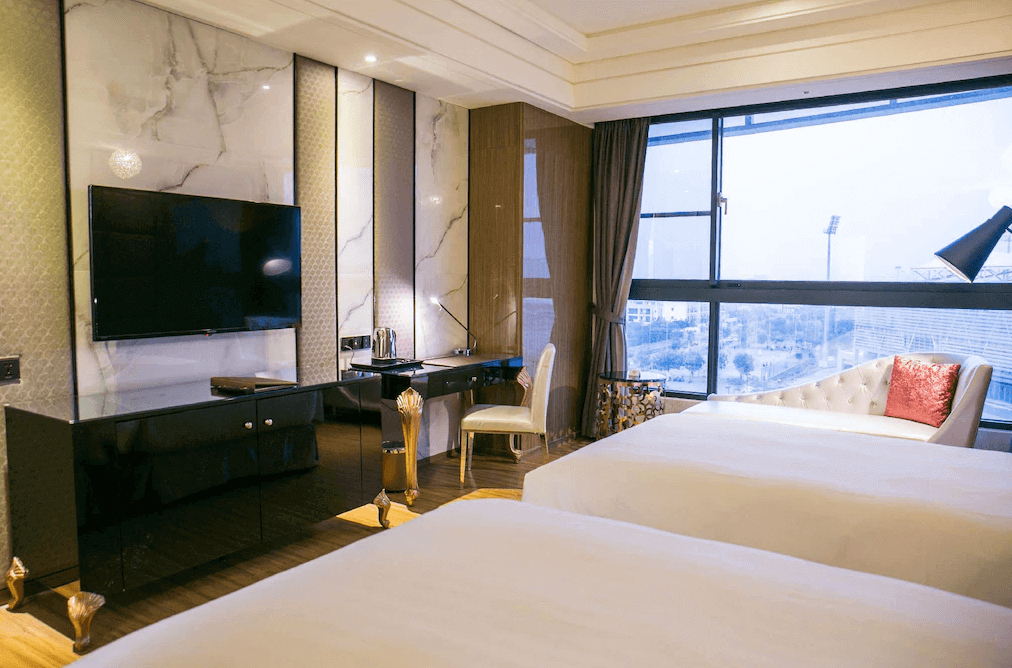 【斗六住宿】三好國際酒店的豪華雙床房，房內配置大片落地窗、典雅梳妝桌、液晶電視與純白高背椅，窗邊擺有貴妃椅與紅色抱枕，營造出舒適又尊貴的入住氛圍。