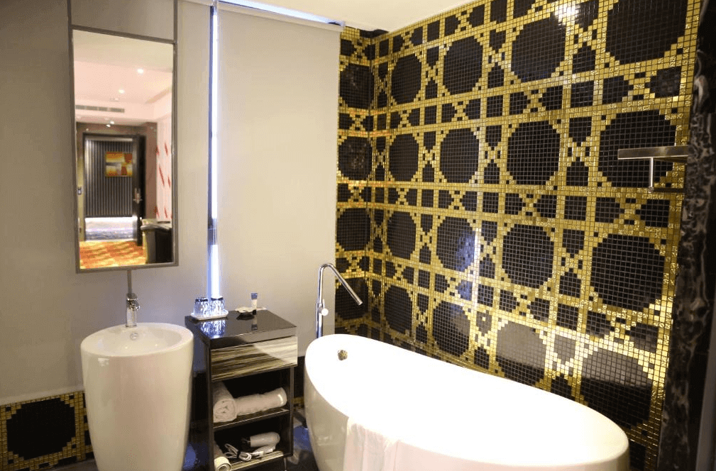 【斗六住宿】三好國際酒店奢華風格浴室，牆面鋪設金黑幾何馬賽克磁磚，配有獨立式蛋形浴缸與立式洗手台，鏡面與燈光設計精緻，呈現現代高雅的沐浴空間。