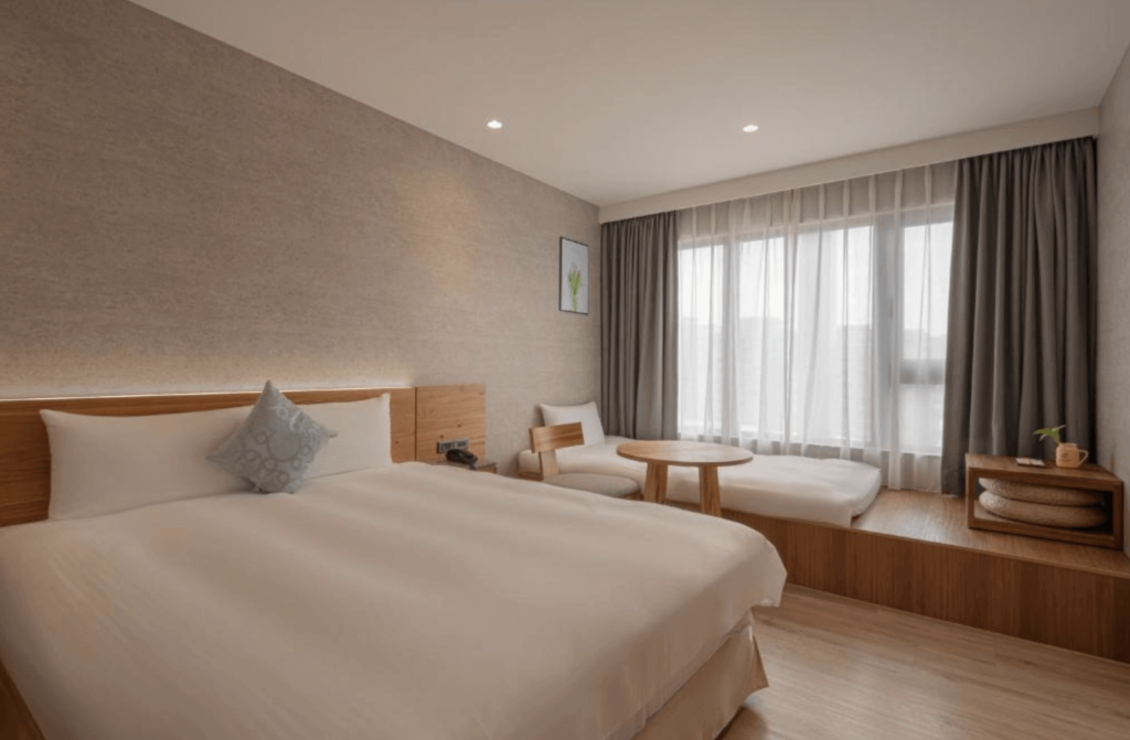 【逢甲夜市住宿】"逢甲夜市住宿精選示意圖"享得道行旅房間以暖色調設計，配有一張舒適的雙人大床與靠窗的和式休憩區，窗邊有坐墊與小茶几，採光柔和，營造出寬敞且溫暖的居住氛圍，適合家庭入住。