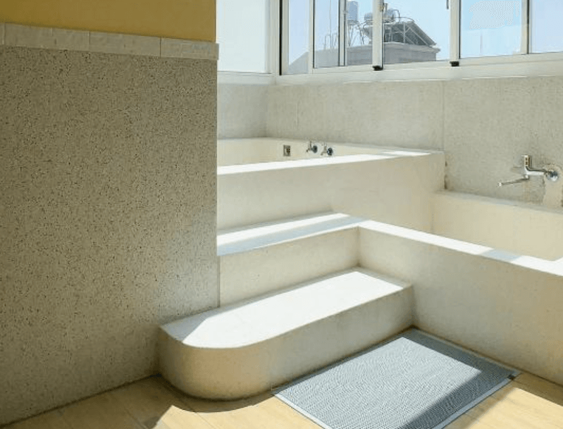 【台南安平住宿】倆倆親子民宿寬敞衛浴空間設有雙層階梯式泡澡池，使用磨石子材質打造，靠窗位置讓沐浴同時享受自然採光。設計簡潔實用，適合親子共浴或放鬆泡澡，呈現溫暖舒適的家庭氛圍。