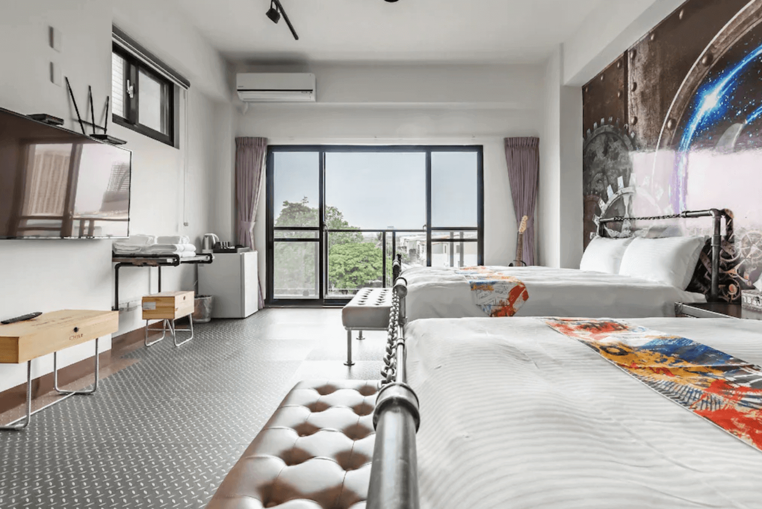 【台南安平住宿】台南搖滾狂民宿採用黑白色調與金屬元素的工業風雙人房，牆面裝飾齒輪與宇宙星球圖案，呈現未來科技感。房內設有兩張雙人床、大型液晶電視、簡易吧檯與基本備品，空間寬敞並附陽台，視野開闊。