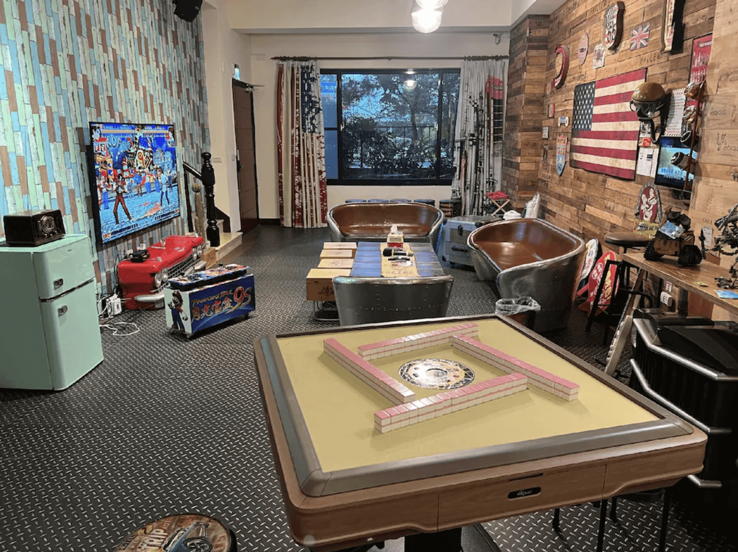 【台南安平住宿】台南搖滾狂民宿的娛樂交誼廳以美式復古元素裝飾，設有美國國旗牆、工業風沙發座椅、全自動麻將桌與電視遊戲機台。空間配置多元，適合朋友聚會、家庭休閒，營造出濃厚的搖滾與自由氣息。