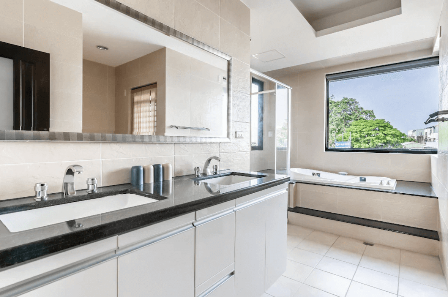 【台南安平住宿】台南搖滾狂民宿的衛浴空間採雙洗手台設計，搭配黑色石材檯面與白色櫃體，乾淨整潔。浴室內另設有大片窗景與嵌入式浴缸，提供舒適的沐浴體驗，適合享受悠閒放鬆時光。