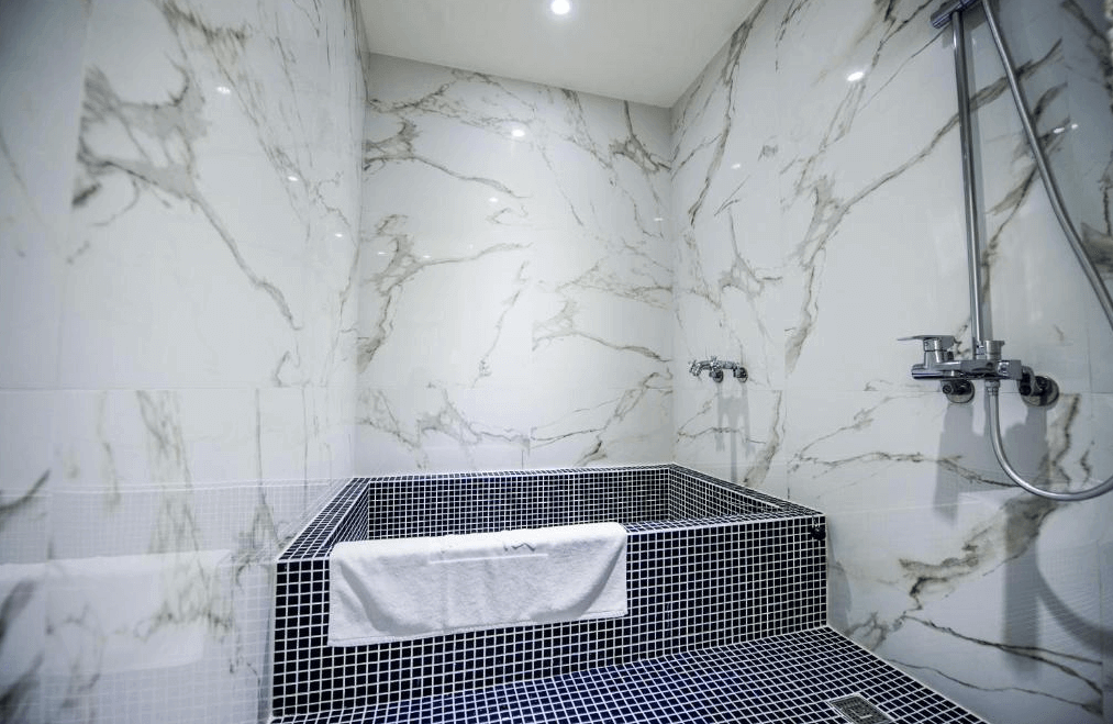 【員林住宿】"彰化飯店"員林紅樓商旅的浴室內部，牆面採用白色大理石紋理磁磚，搭配黑色小方磚浴池，提供深度泡湯的功能。浴室內附設蓮蓬頭與雙水龍頭，整體風格簡潔而高級。