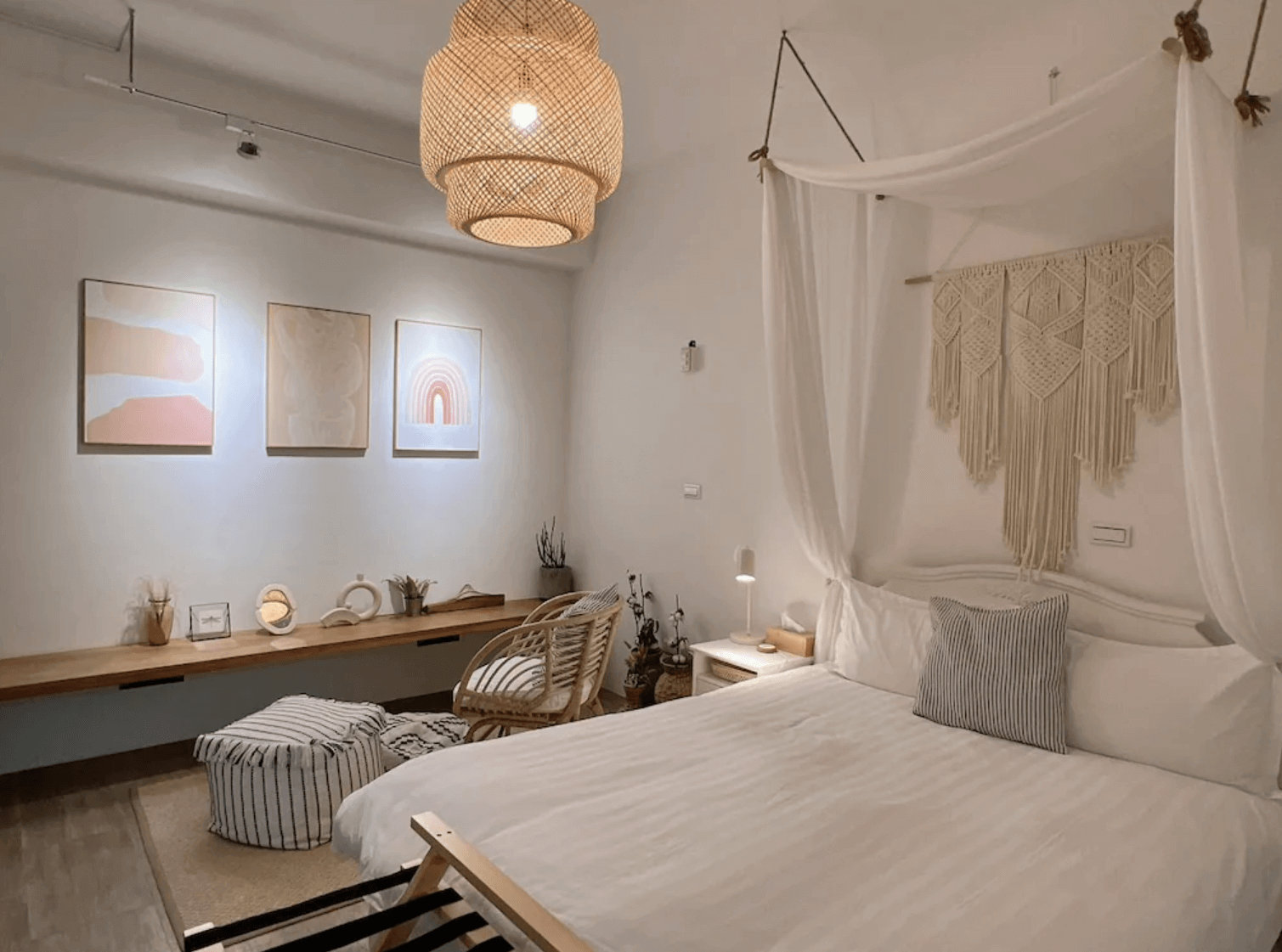 【台南安平住宿】四季洋房的房間以米白與淺木色為主調，配上編織掛飾與紗帳床柱，展現出濃厚的波希米亞風格。牆上掛有柔和色調的藝術畫作，搭配藤編燈飾與座椅，營造出靜謐放鬆的藝術氛圍。