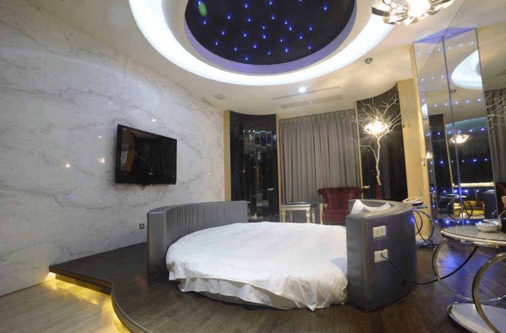 【斗六住宿】天上人間精品旅館的圓床房型，床鋪置於微微抬高的木平台上方，天花板有藍色星光燈飾，牆面為大理石紋理，房內搭配紅色沙發與鏡面裝飾，整體設計前衛又浪漫。