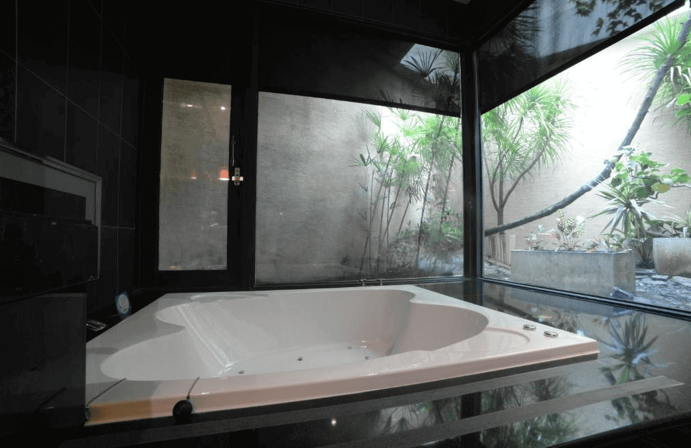 【斗六住宿】天上人間精品旅館的浴室，設有一座大型按摩浴缸，三面玻璃窗可見綠意植栽造景，空間採黑色瓷磚與落地窗設計，營造出放鬆且私密的沐浴環境。
