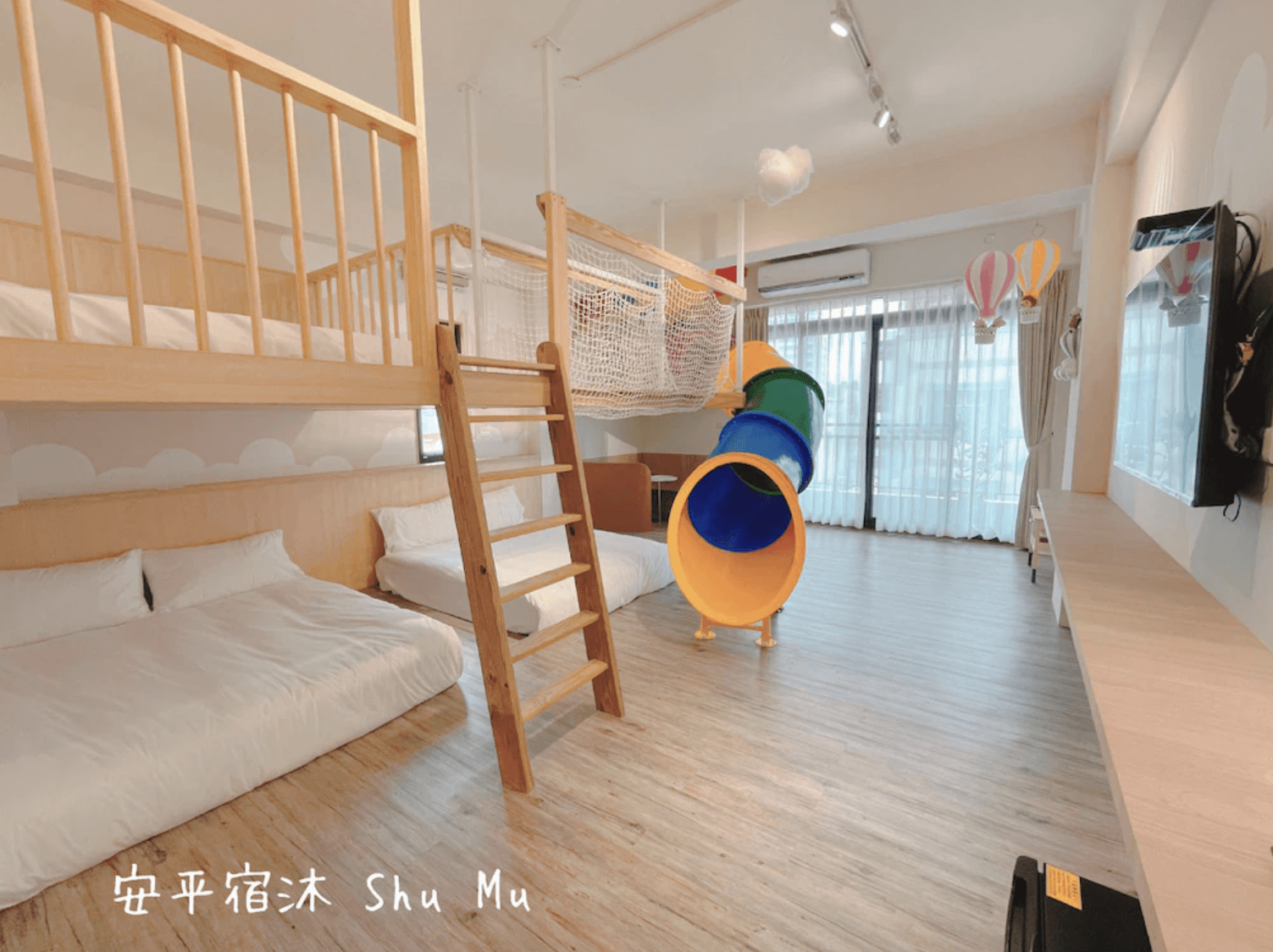 【台南安平住宿】安平宿沐的親子房設有上下舖雙人床，並設有室內溜滑梯與吊床網架，讓小朋友可在房內安全放電。整體空間寬敞明亮，天花板掛有熱氣球裝飾，富有冒險與夢幻感。
