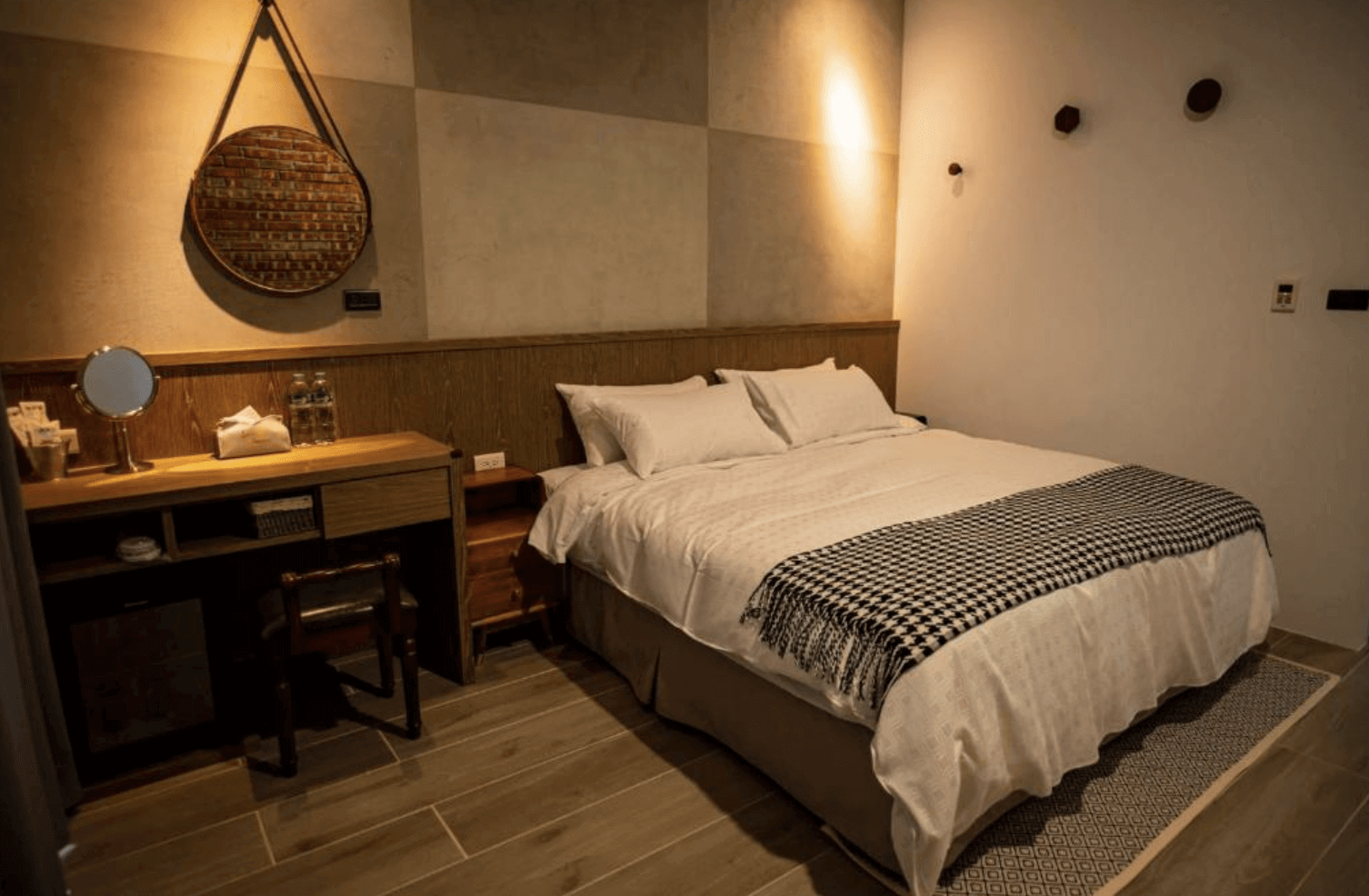 【台南安平住宿】安平有間旅店的雙人房，配有柔和燈光、木質地板與簡約設計的梳妝台，床鋪擺設整齊，牆面裝飾圓形鏡與幾何線條，展現簡約工業風格。