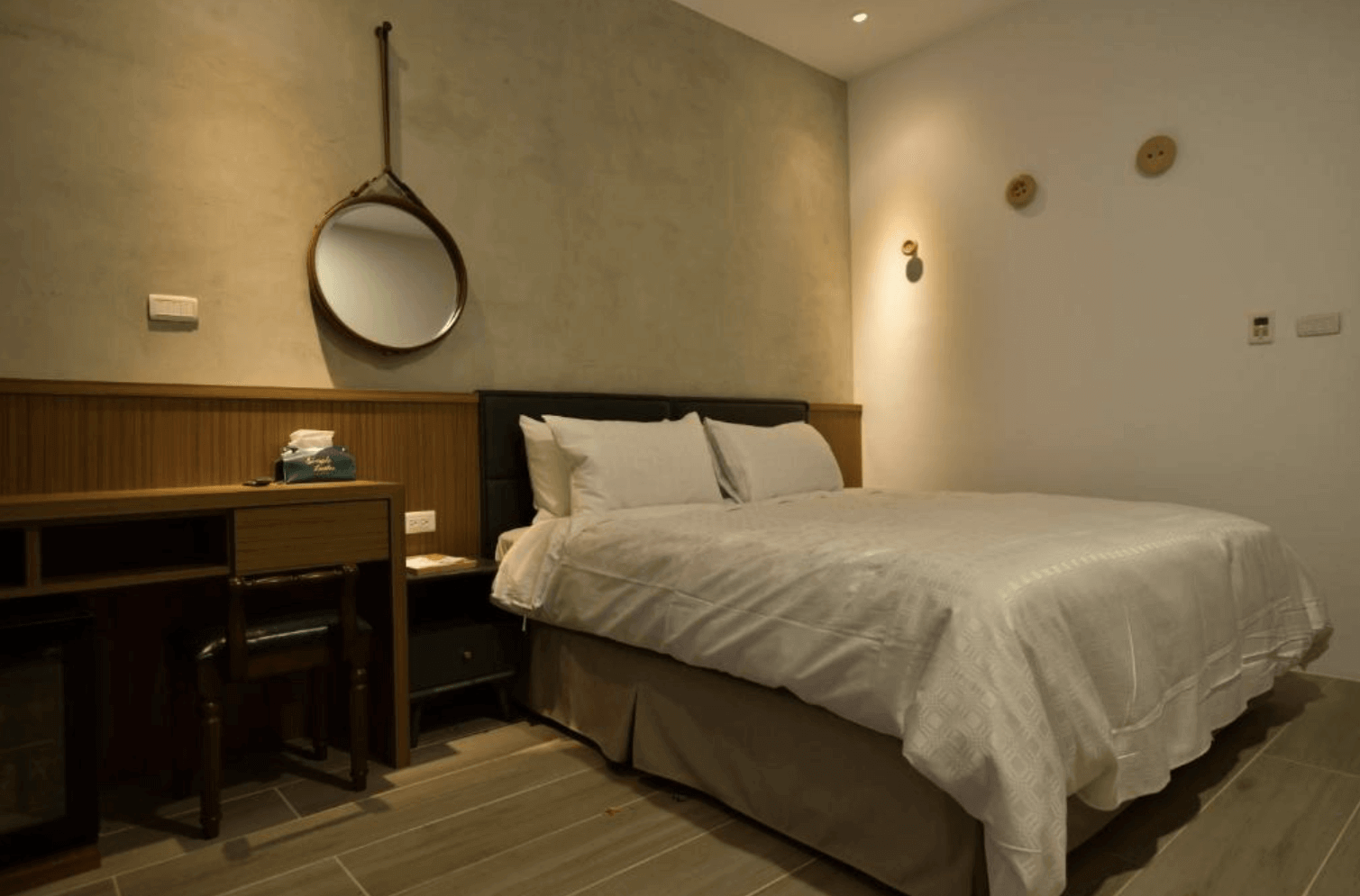 【台南安平住宿】安平有間旅店的雙人房，牆面懸掛圓形皮帶鏡，搭配木質梳妝台與皮椅，整體採低調的灰與米色系營造沉穩舒適的住宿空間。