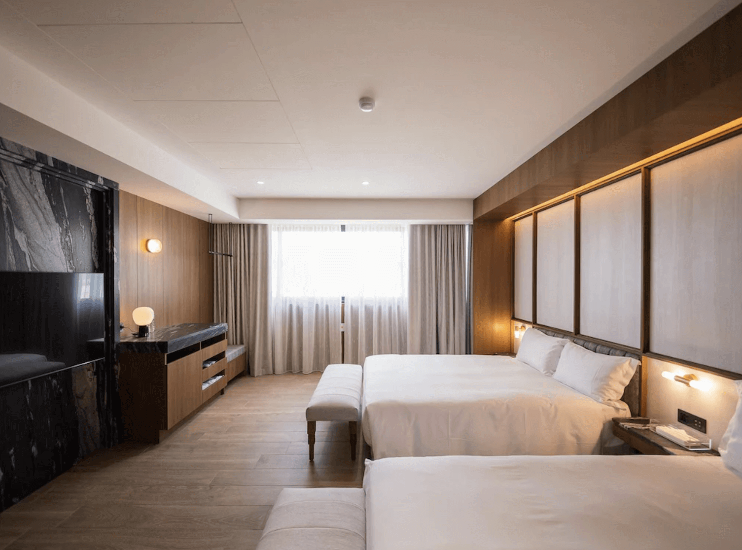 【台南安平住宿】安平留飯店的雙床房，房間內設有兩張大床與長椅，牆面採用木質與柔和燈光設計，搭配大理石質感的電視牆與書桌，營造沉穩高雅的住宿氛圍。