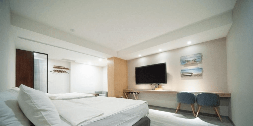 【虎尾住宿】小9窩BNB的雙人房，牆上掛有兩幅海邊風景畫，設有平面電視與長型木質書桌，雙張藍色椅子增添色彩，燈光柔和營造溫暖住宿體驗。