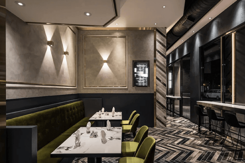 【高雄親子飯店】帕可麗酒店高雅時尚的餐廳空間，以黑金色調搭配綠色絲絨座椅，展現精緻感。餐桌為大理石桌面，擺放著整齊的餐具與餐巾，營造高級用餐體驗。牆面燈光設計巧妙，增添溫暖氛圍，並提供吧檯座位，適合不同用餐需求。