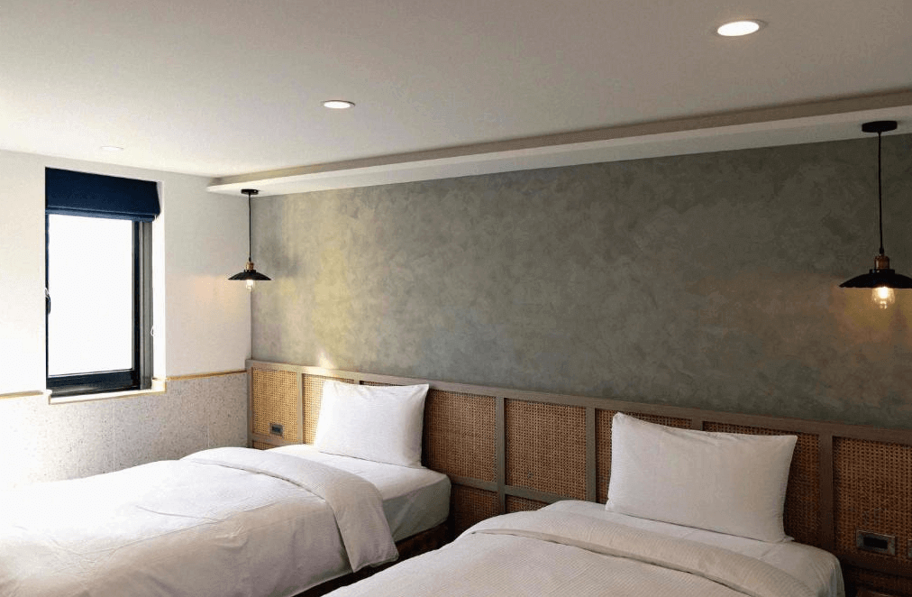 【員林住宿】康橋商旅-員林館的雙床房型，設計風格現代簡約，床頭採用編織藤編元素，搭配灰色質感牆面與暖色吊燈，展現獨特的工業風與自然風融合。房內有一扇窗戶，可引入自然光，整體環境舒適清新。