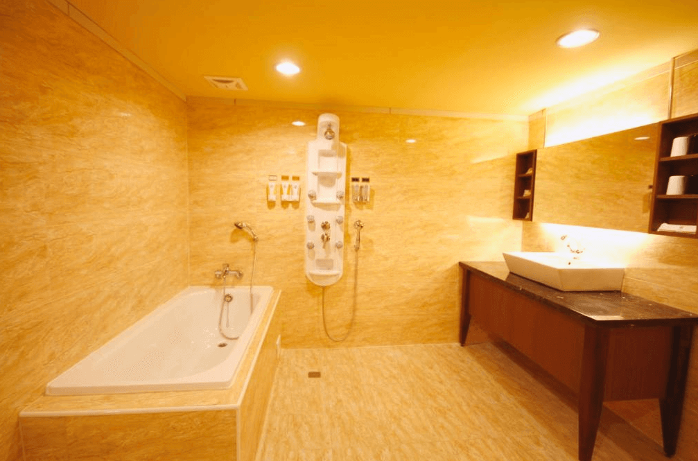 【員林住宿】康橋商旅-員林館的浴室，採用大理石紋路的金黃色磁磚設計，內有獨立浴缸與淋浴設備，並配備多功能按摩花灑。洗手台設於黑色石材檯面上，整體空間寬敞且燈光溫暖，營造高級感。