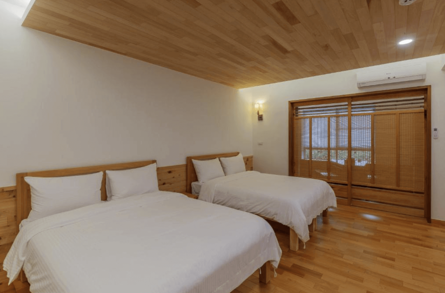 【鹿野住宿】後山人家民宿A館的日式風格房間，兩張雙人床搭配木製床頭板，整體色調溫暖柔和。房內設有大片木質拉門，通往陽台區域，窗外景色宜人。設計簡約但充滿日式禪意，適合喜愛和風設計的旅客。