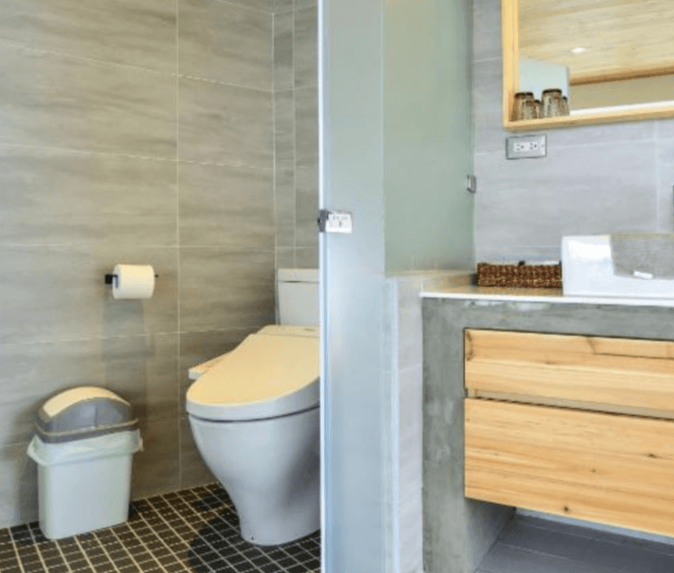 【台南安平住宿】思慕嶼 微光旅行的衛浴空間，使用灰色磁磚與霧面玻璃隔間，配置免治馬桶與獨立洗手台，搭配木質抽屜與大鏡面，呈現簡潔又自然的設計感。