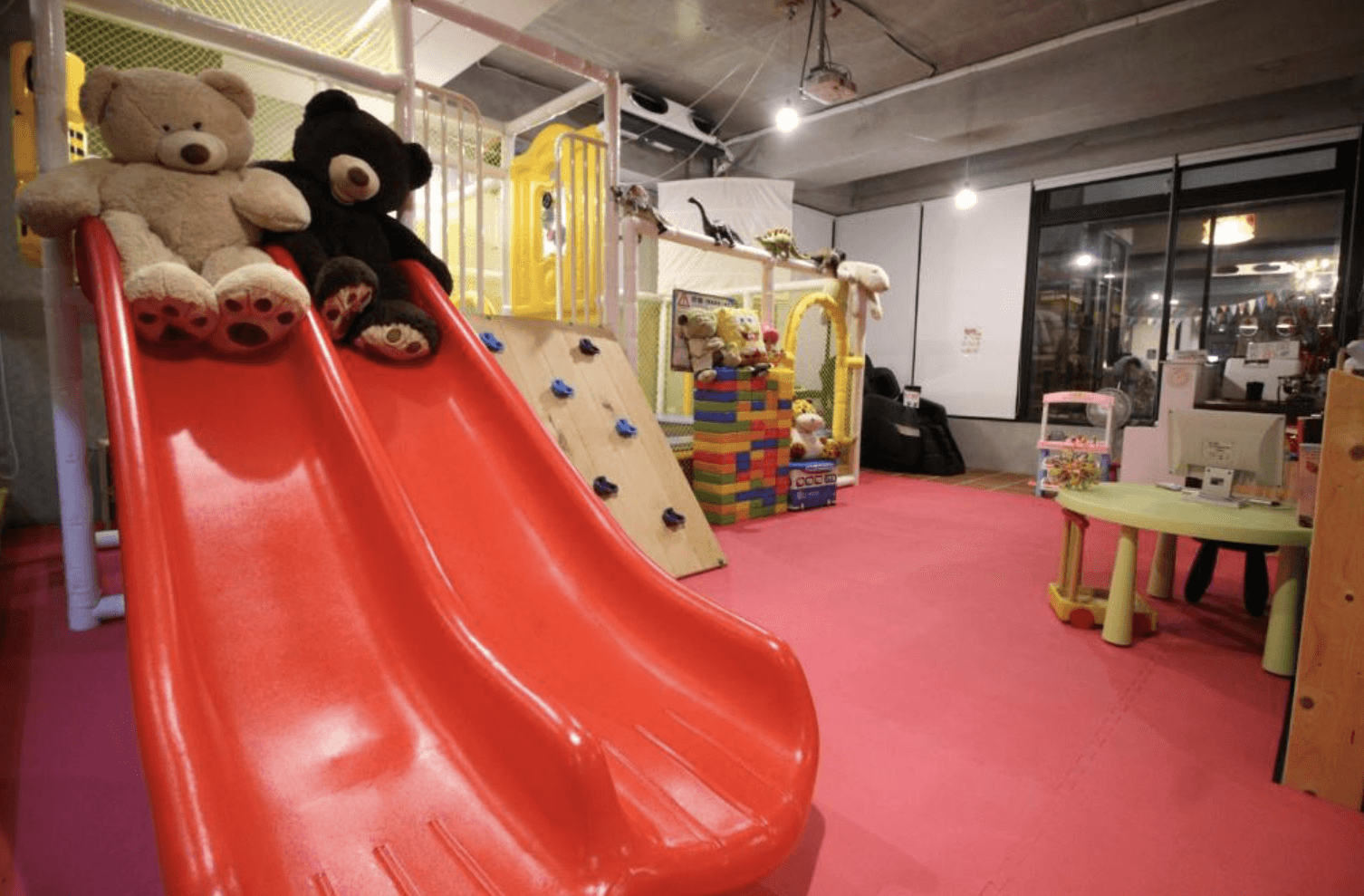 【台南安平住宿】我小時候設計旅店的室內兒童遊戲區，鋪有粉紅色安全地墊，設有雙人溜滑梯、攀岩牆與大型積木區，周圍擺滿玩偶與玩具，打造友善親子的遊戲環境。