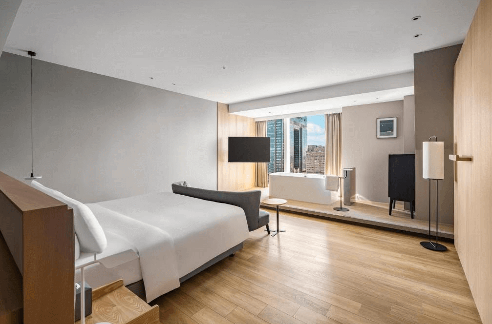 【高雄親子飯店】承億酒店的高級客房，採用開放式設計，房內設有獨立浴缸並可欣賞都市天際線。木質地板與現代感十足的家具相結合，營造高雅舒適的住宿環境。床旁設有小型沙發與圓桌，適合休憩或閱讀。