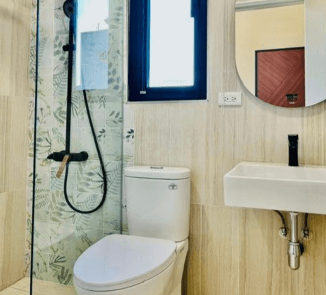 【虎尾住宿】日日見宅的衛浴空間採木紋與葉子圖樣磁磚拼接設計，設有乾濕分離淋浴間、白色馬桶與方形洗手台，搭配圓形鏡子，整潔清新。