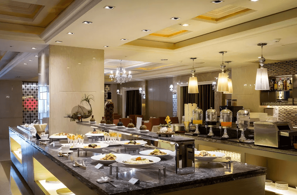 【員林住宿】"彰化飯店"昇財麗禧酒店飯店自助餐廳，裝潢高貴典雅，設有大理石餐檯與水晶吊燈，提供豐富的自助餐點。飲料區擺放多種果汁，並有精緻擺盤的各式料理，營造豪華用餐氛圍。