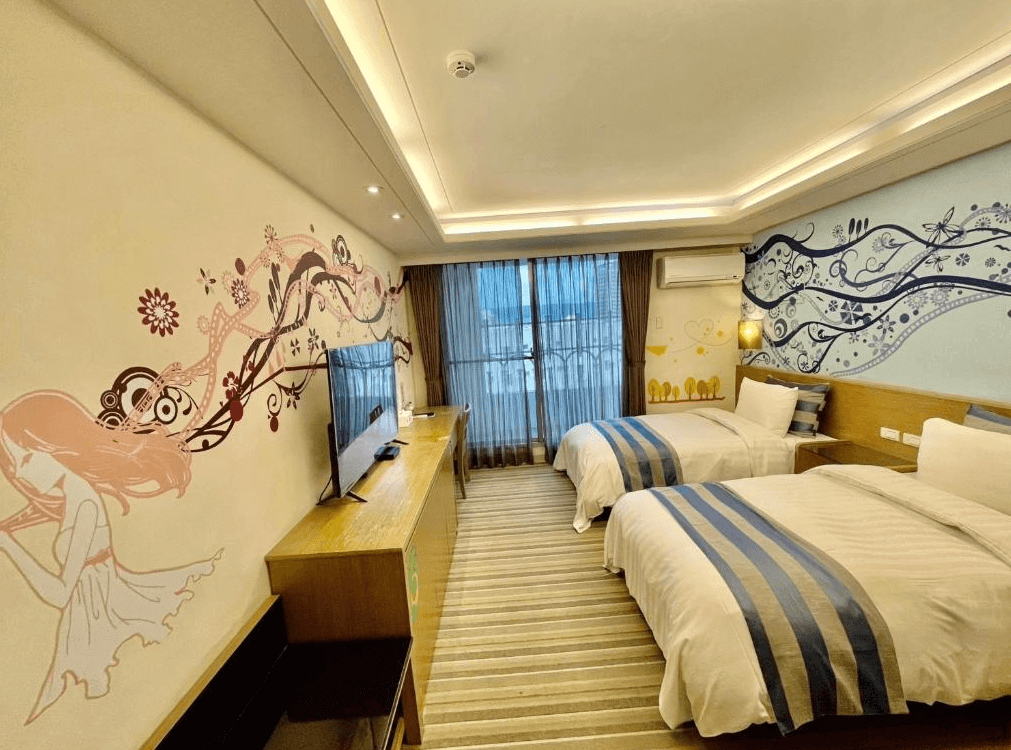 【員林住宿】晨陽文旅的兒童友善主題房，牆面裝飾童趣風格壁畫，搭配雙床設計，適合親子入住。床頭牆面運用粉色與藍色圖案點綴，展現活潑氛圍，並設有大面落地窗，引入自然光線。