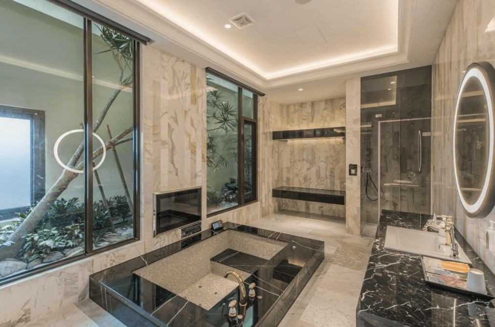 【員林住宿】棕櫚湖岸精品旅館的豪華浴室空間，採用大理石紋理牆面與黑色石材浴池，搭配嵌入式燈光設計，營造高級水療感。浴室設有大片落地窗，引入自然光與庭院綠意，並附有雙洗手台與圓形背光鏡，展現現代感與功能性。