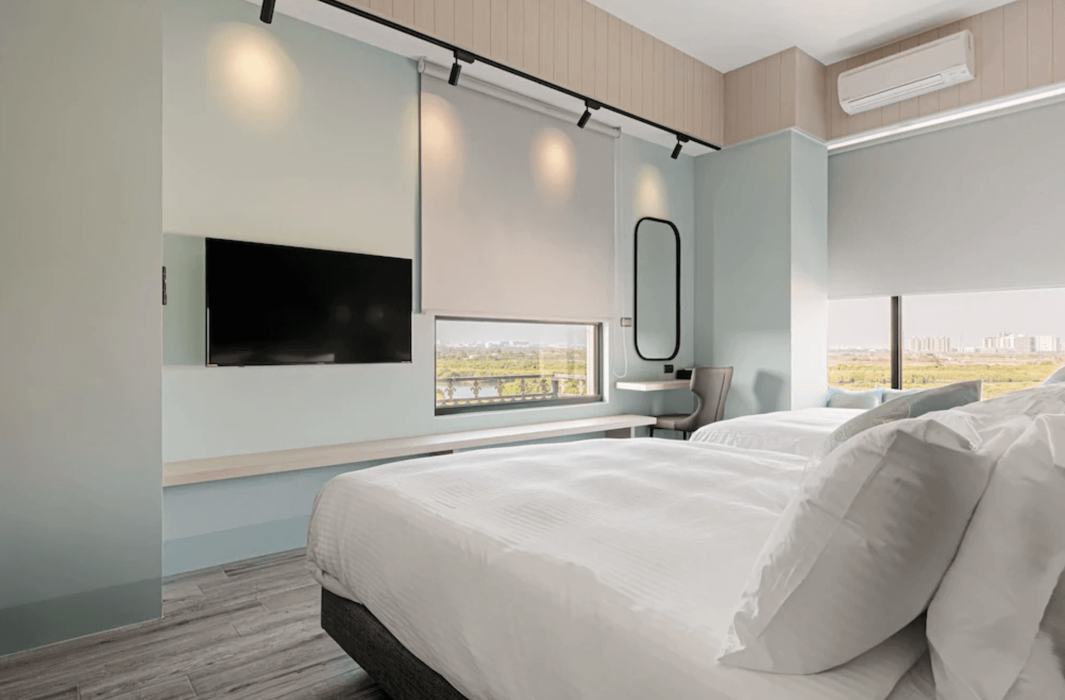 【台南安平住宿】森行旅以淡藍色調為主軸的房型，搭配大片窗景可遠眺綠意河岸，房內設有兩張雙人床、大型液晶電視與化妝鏡桌，簡約設計結合自然光，營造出開闊且明亮的休憩空間。