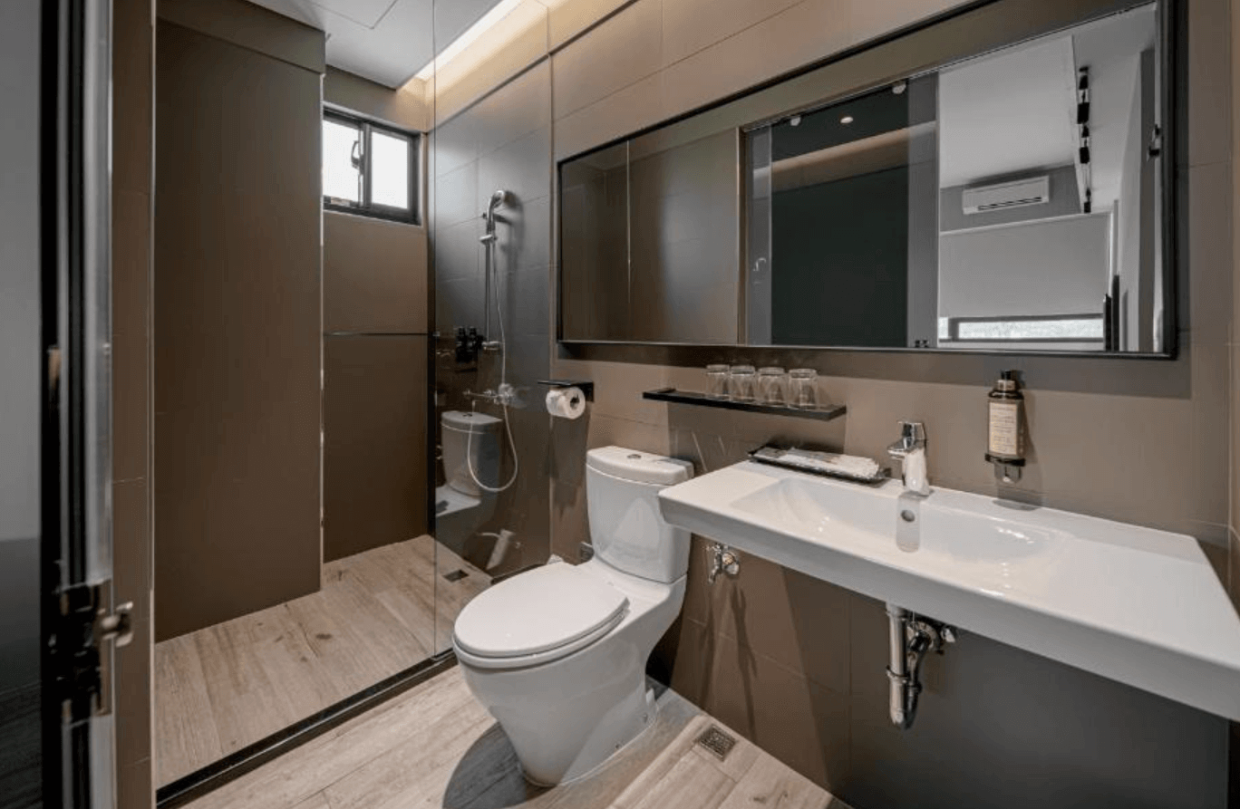 【台南安平住宿】森行旅乾濕分離設計的衛浴空間採用深色瓷磚與玻璃隔間，搭配長型鏡面與白色洗手台，簡潔俐落。備有基本衛浴用品與杯具，整體清潔明亮，展現高質感旅宿標準。