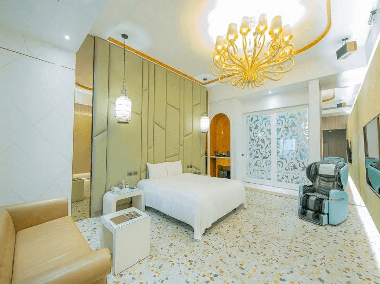 【員林住宿】楓采時尚汽車旅館奢華風格的飯店房間，白色與金色為主調，搭配水磨石地板與雕花玻璃屏風，增添精緻感。房內擺設白色大床、皮質沙發、吊燈以及按摩椅，提供高級享受與舒適的住宿體驗。